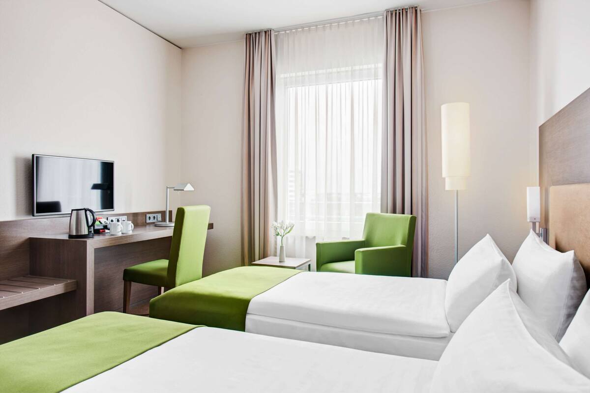 A hotel room with two beds, a desk with a flat-screen TV, a coffee maker, and a lamp.