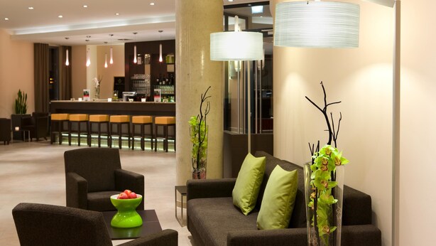 Un vestíbulo moderno con sofá, sillas, zona de bar y plantas decorativas.