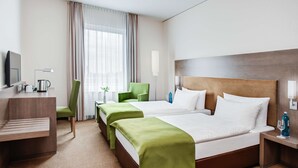 Habitación de hotel con dos camas, un escritorio, una silla, un televisor y una ventana con cortinas.