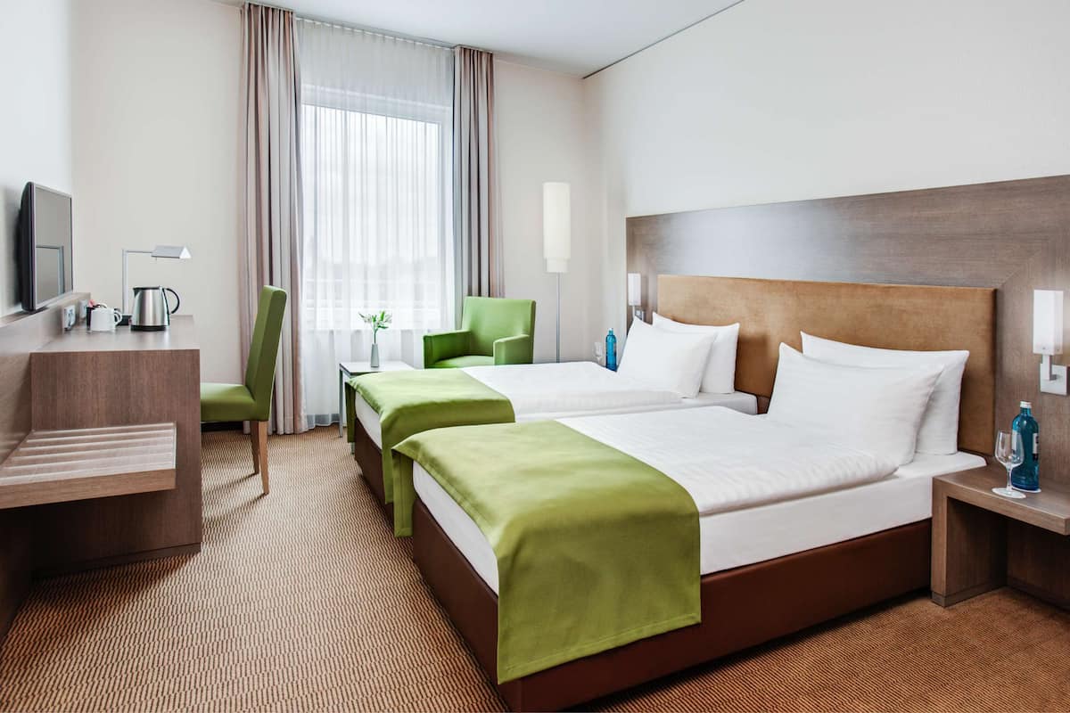 A hotel room with two beds, a desk, a chair, a TV, and a window with curtains.