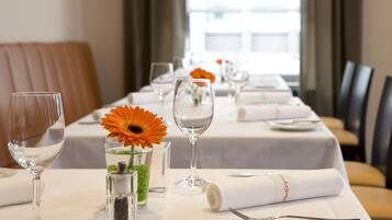 Une table de restaurant d’hôtel, mise avec des verres à vin, un vase de fleurs et des serviettes soigneusement pliées.