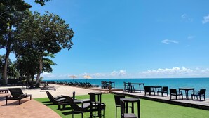 Un área de descanso junto a la playa con sillones y mesas, una sección de césped artificial verde y vista al océano.