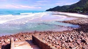 Una playa con agua cristalina, costa rocosa y una escalera que baja a la playa.