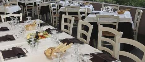 A restaurant with outdoor seating, white tables, and chairs, set against a backdrop of greenery and a distant view.
