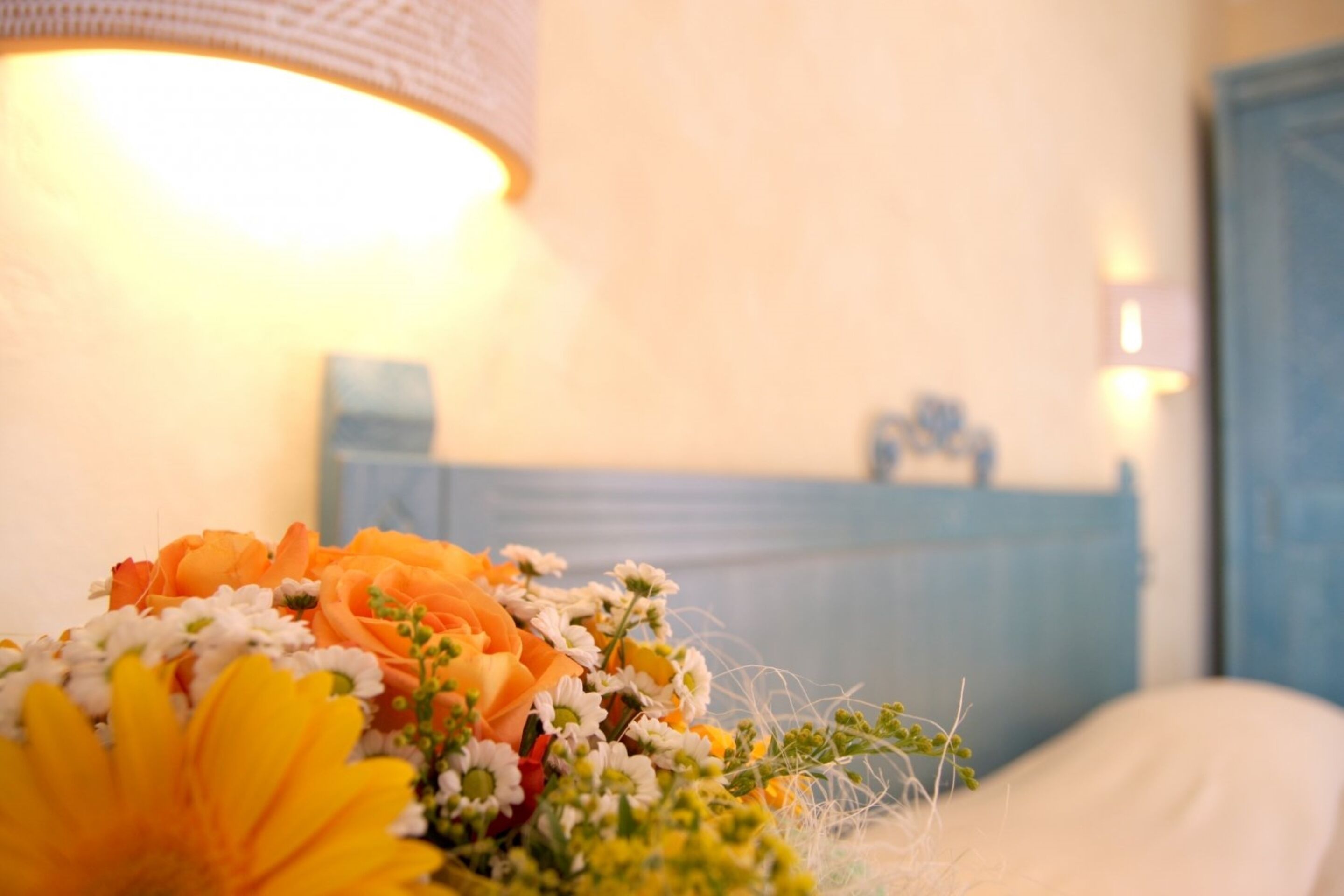 A bouquet of flowers on a bedside table with a lamp in the background.