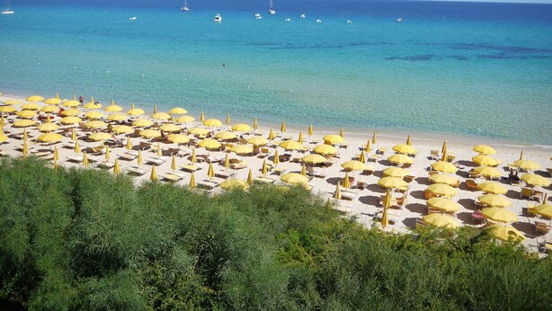 A beach with numerous yellow umbrellas and sun loungers, a clear blue sea, and boats in the distance. - TH Costa Rei - Free Beach Club (Muravera)