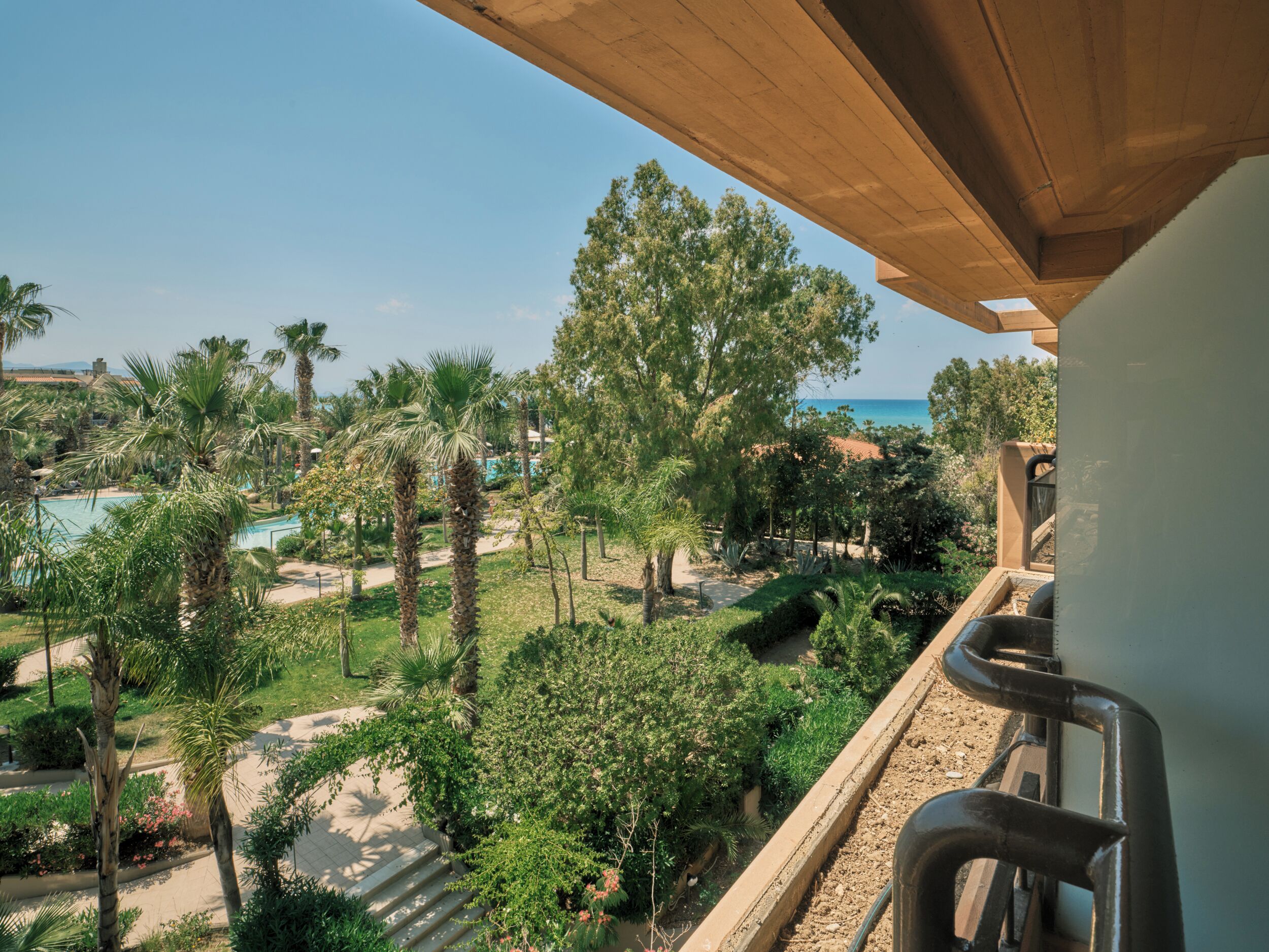 A balcony with a view of a pool, palm trees, and a clear sky.