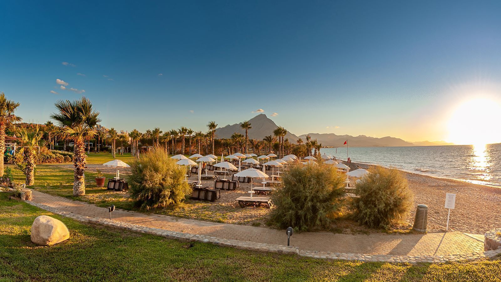 A beachside resort with sun loungers, umbrellas, and a view of the sea and mountains.