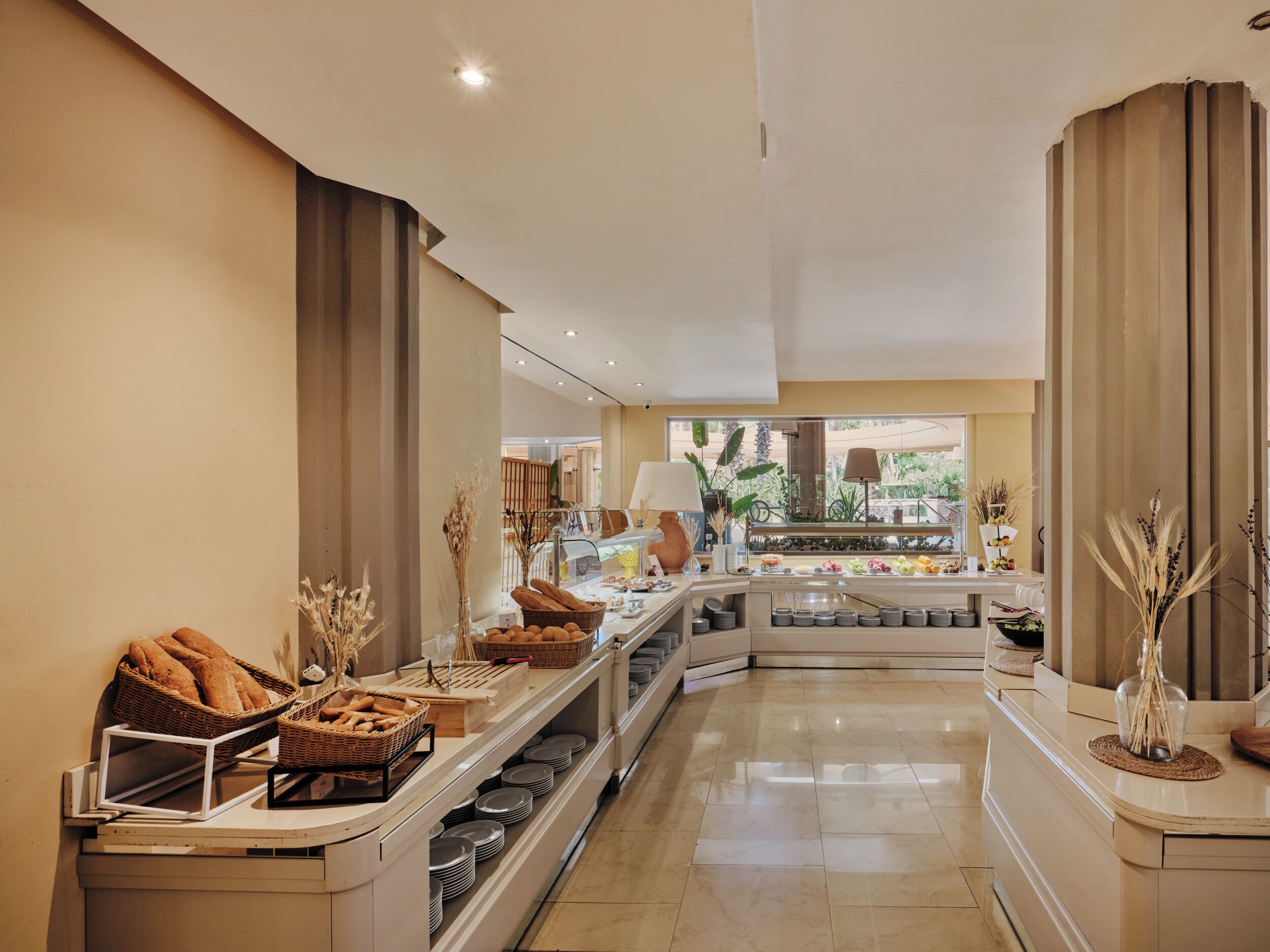 Zona de desayuno de hotel con barra de buffet, que incluye pan, bollería y una variedad de platos.