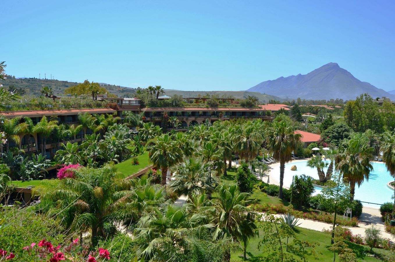 A resort with a pool, palm trees, and a mountain in the background.