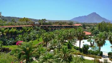 A resort with a pool, palm trees, and a mountain in the background.