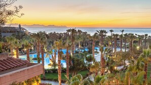 A resort with a pool area, palm trees, and a view of the ocean at sunset. - Acacia Resort (Campofelice di Roccella)