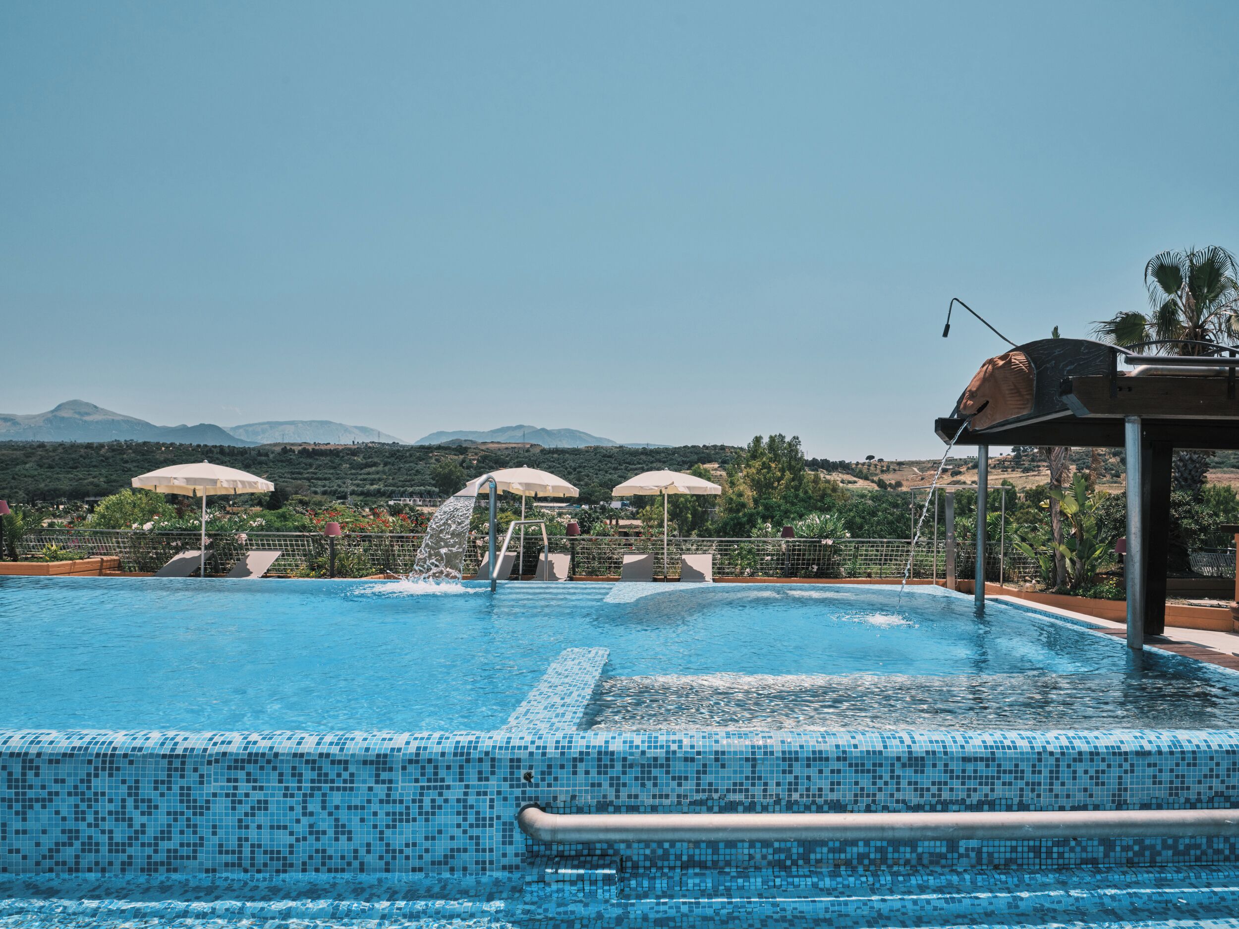 A swimming pool with a view of mountains, a water slide, and umbrellas.