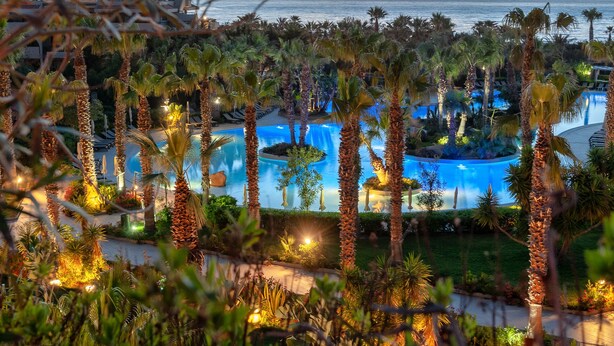 A resort with multiple swimming pools surrounded by palm trees and a view of the ocean at sunset. - Acacia Resort (Campofelice di Roccella)