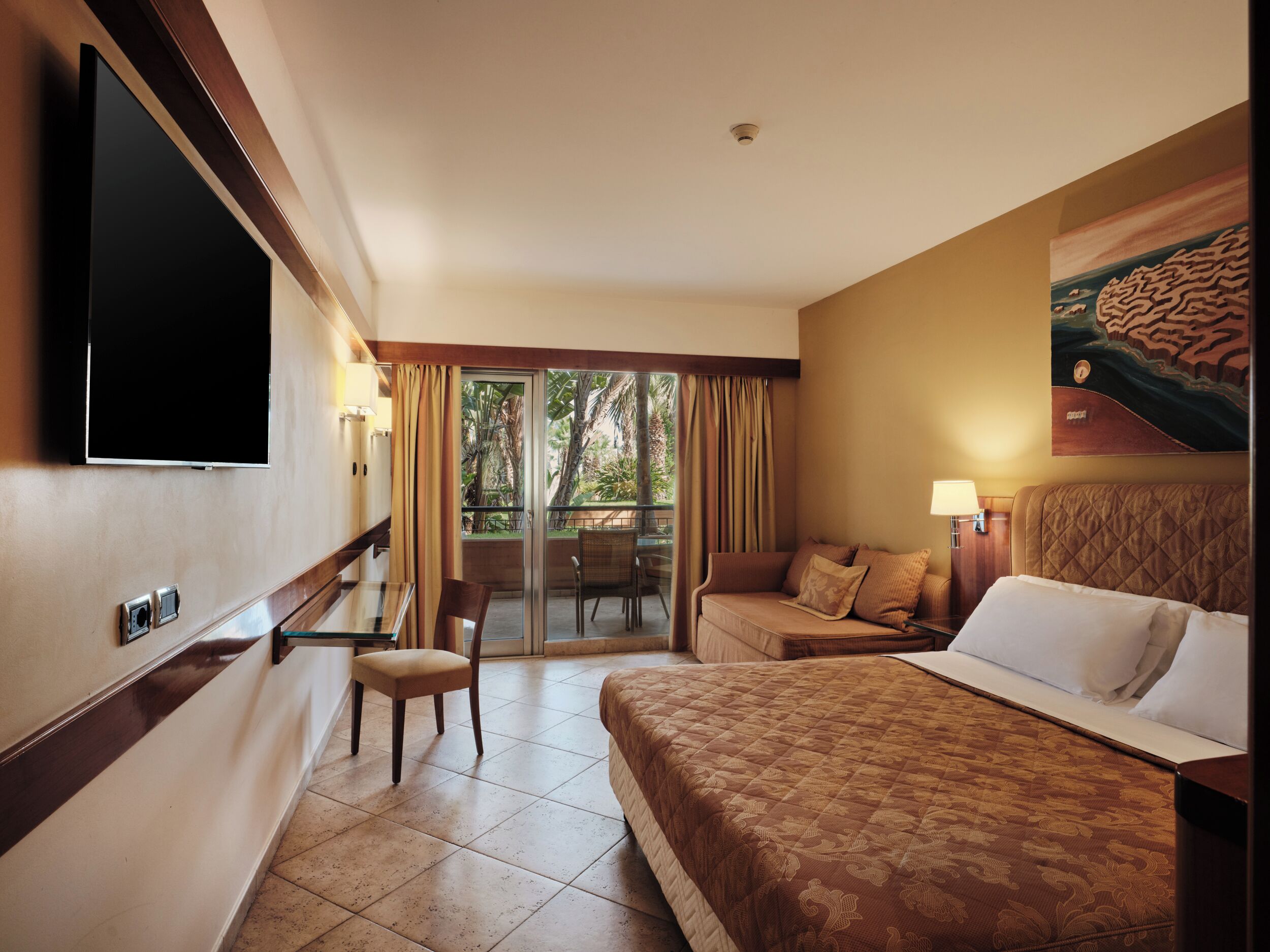 Une chambre d’hôtel comprenant un lit, un canapé, une chaise, une télévision et un balcon avec des rideaux.