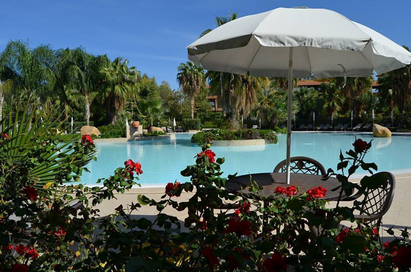 Un espace piscine agrémenté d’un parasol blanc, entouré d’une végétation luxuriante et de fleurs rouges.