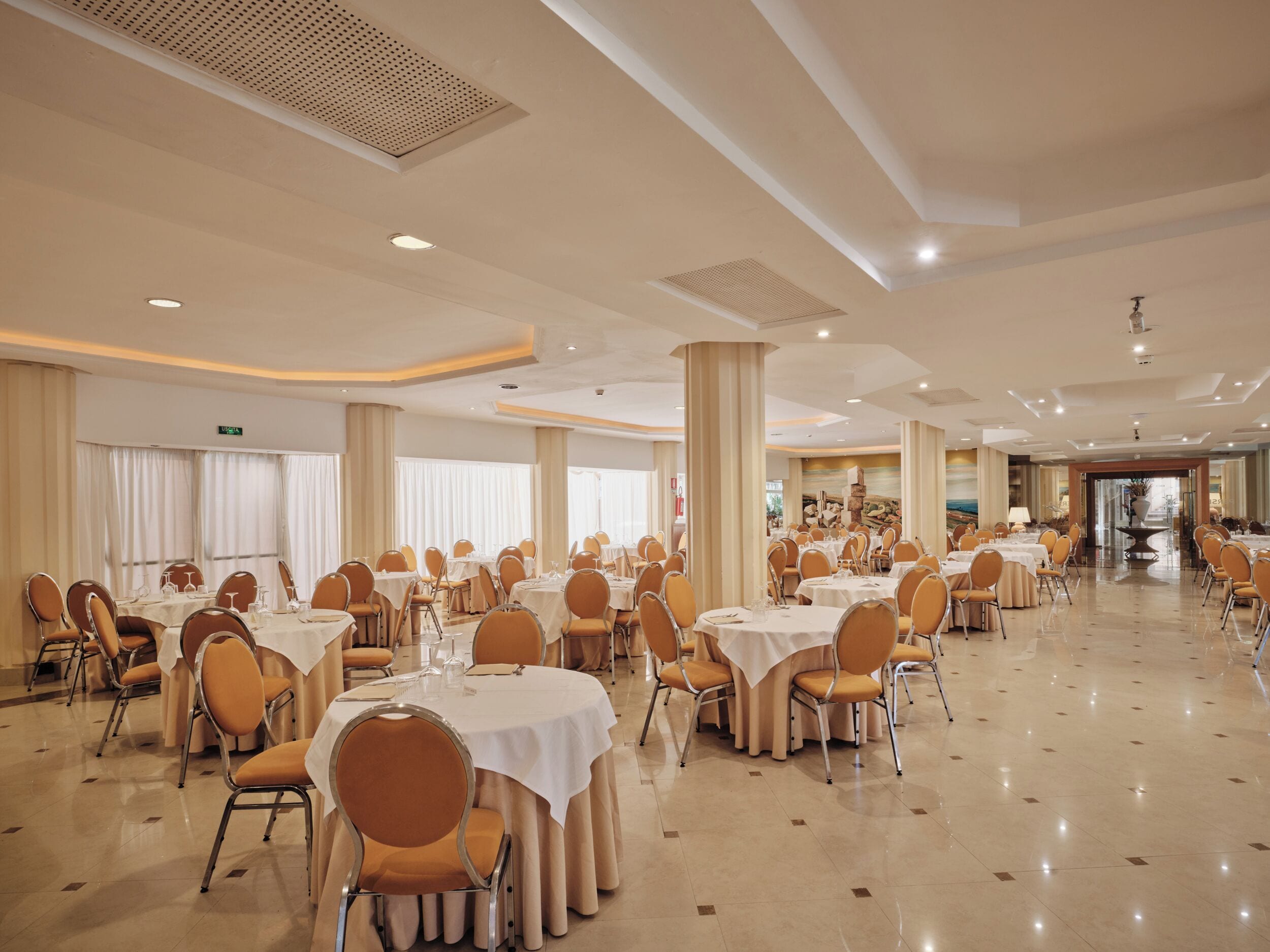 A spacious banquet hall with multiple round tables, chairs, and a polished floor.