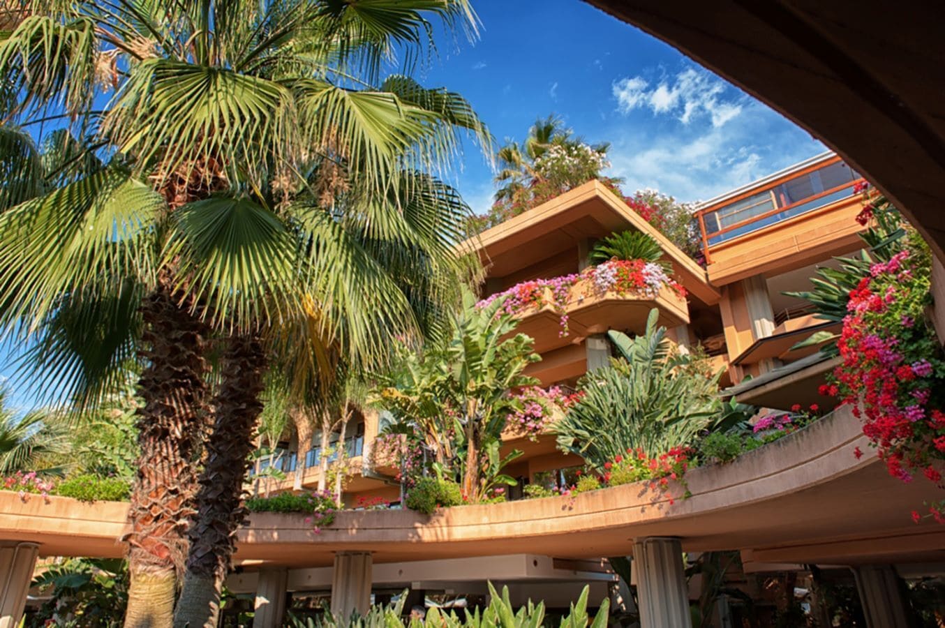 A hotel with a multi-level structure, outdoor balconies with flower planters, and palm trees.
