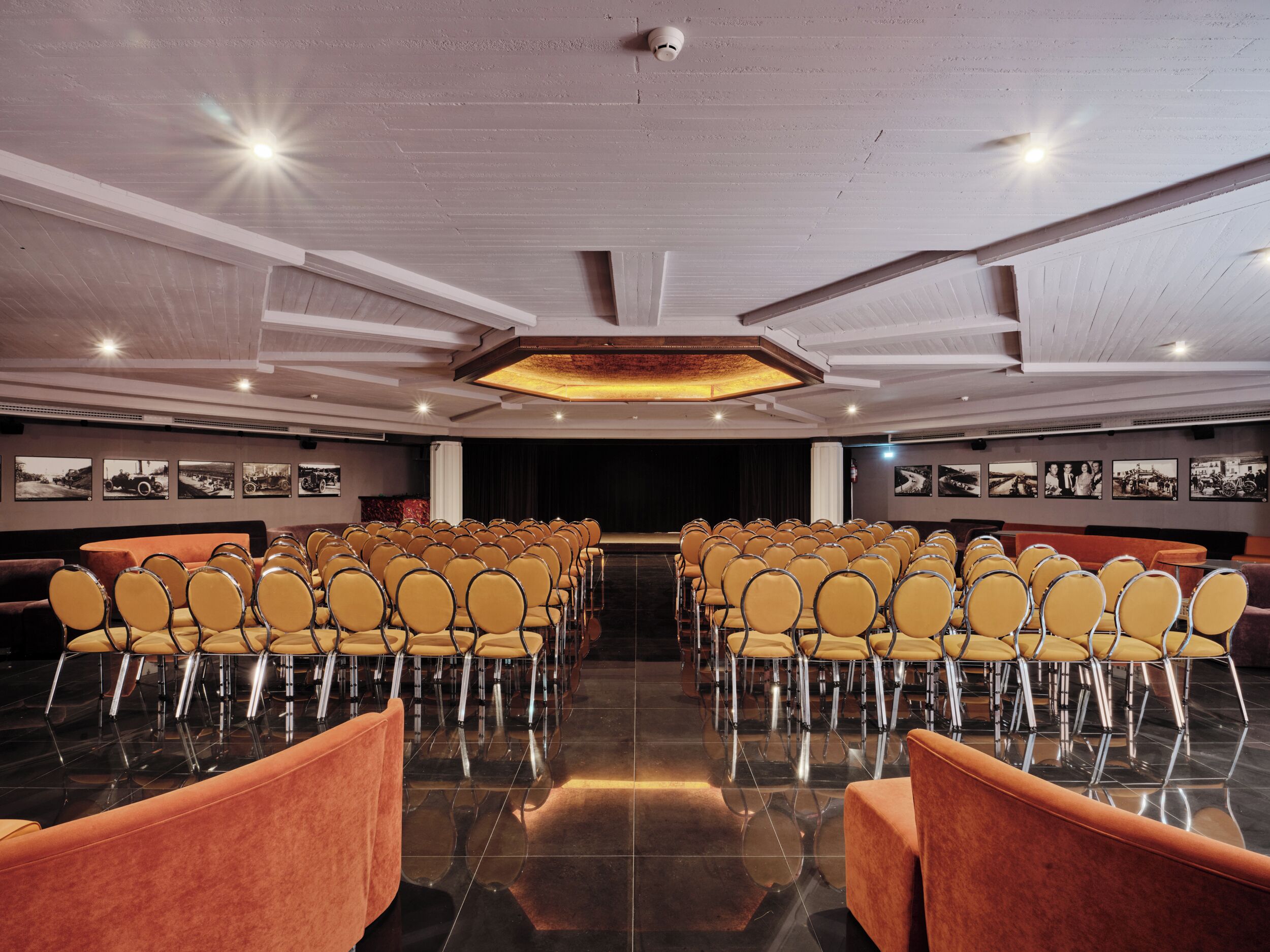 Une salle de conférence avec des rangées de chaises, une scène et un plafond doté d’un éclairage encastré.
