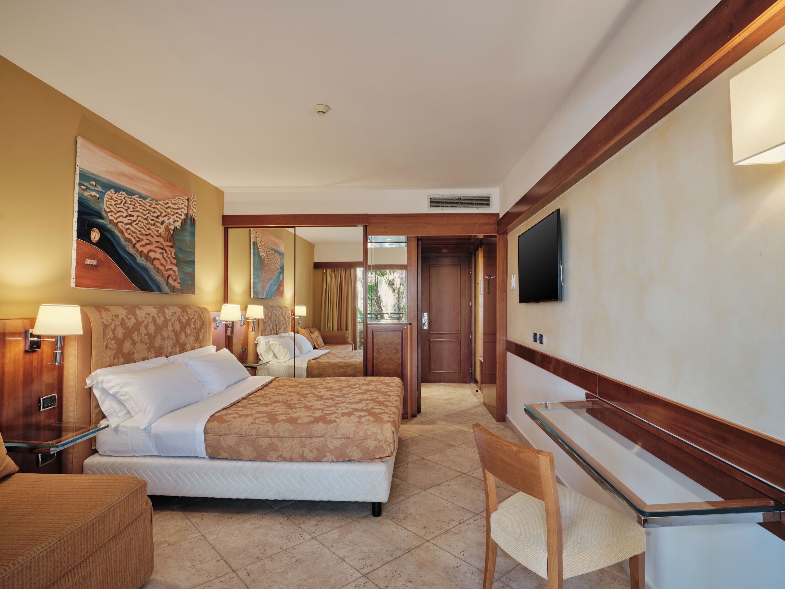 A hotel room with a bed, a desk, a chair, a television, and artwork on the walls.