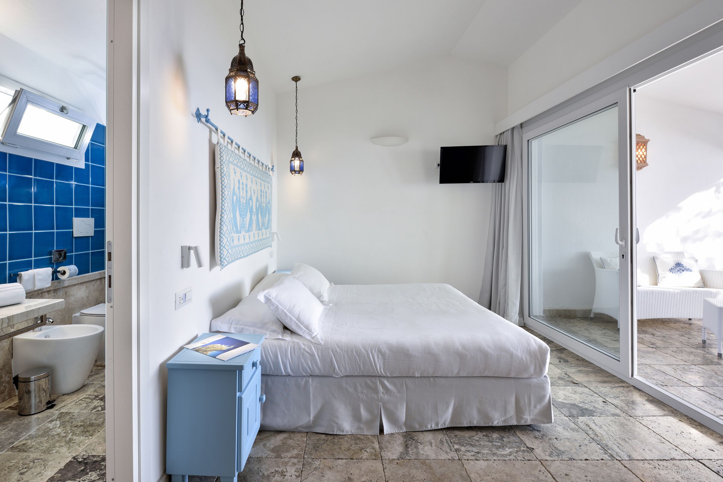 Un dormitorio moderno con una cama grande, un baño con azulejos azules y un balcón con puerta de cristal corredera.