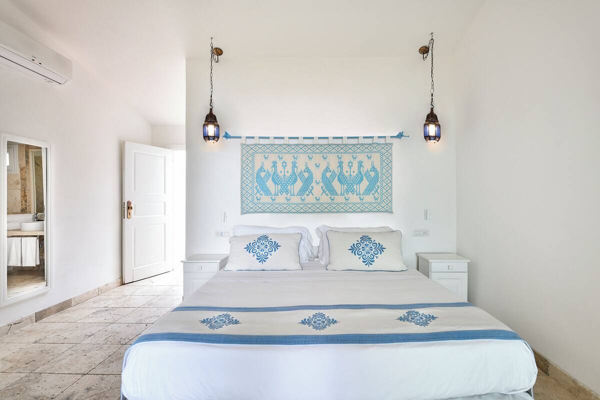 Une chambre à coucher avec un grand lit, deux tables de chevet, un luminaire fixé au mur et une tapisserie à motifs au-dessus du lit.