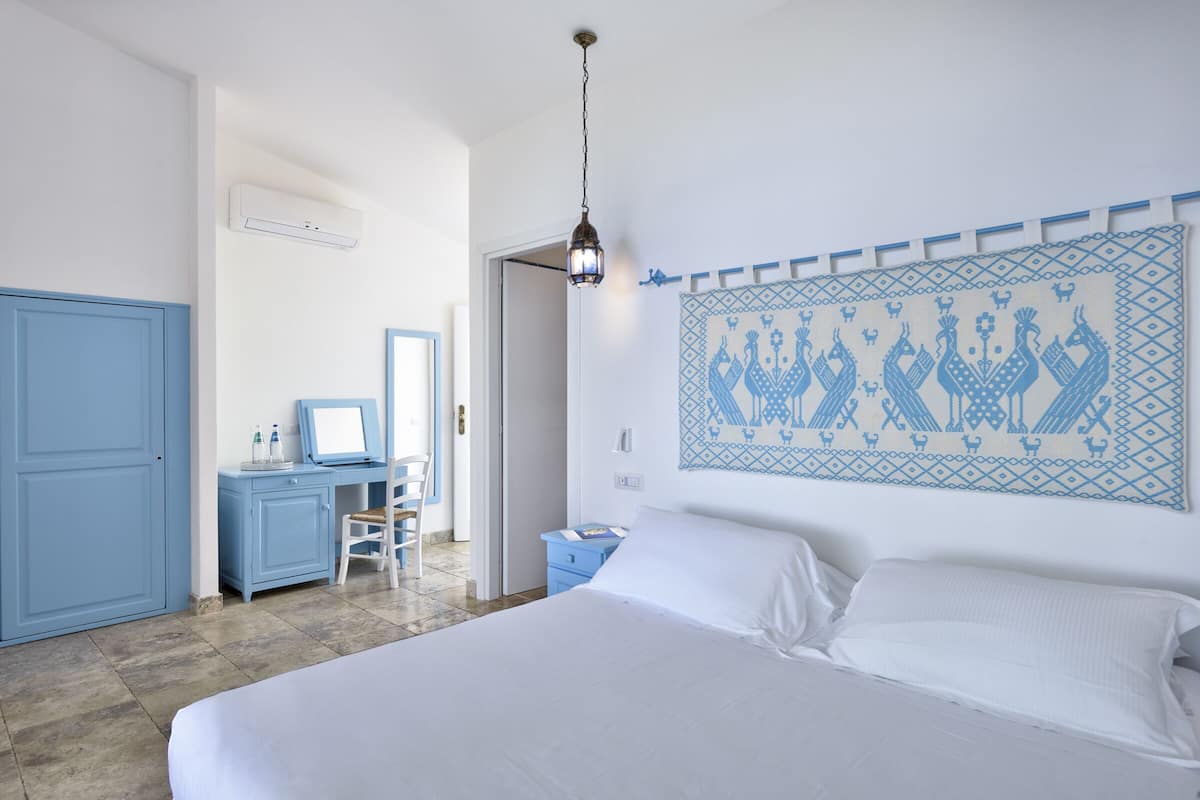 Une chambre avec un grand lit, un bureau avec une chaise, une armoire et un climatiseur fixé au mur.