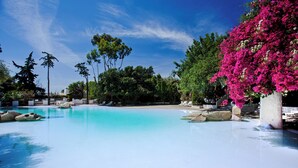 A clear blue pool surrounded by lush greenery and pink bougainvillea flowers. - Arbatax Park Resort - Telis by Falkensteiner (Tortoli)