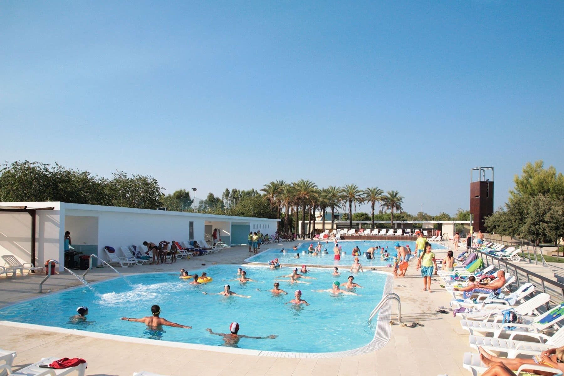 Una piscina con diverse corsie, lettini prendisole e una torretta per il bagnino.