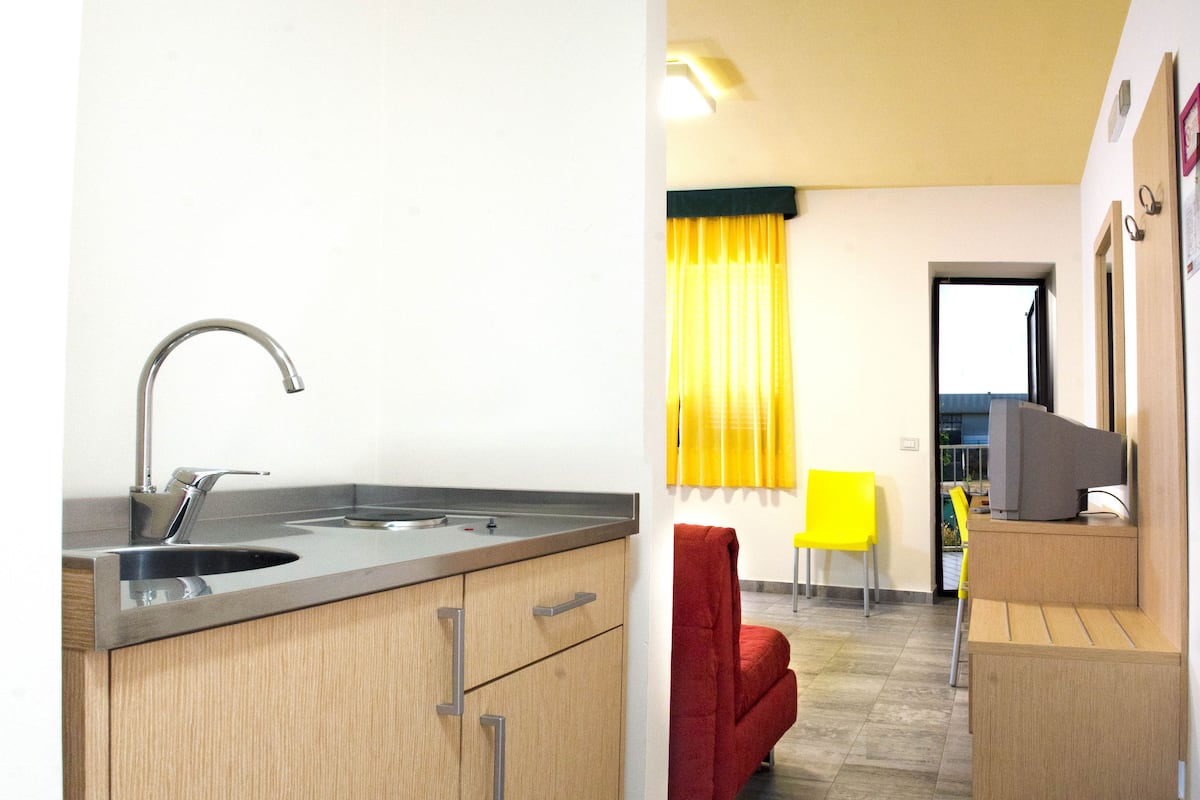 Una cocina compacta con un grifo moderno, armarios de madera y una silla roja.