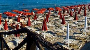 A beach with rows of sun loungers and red umbrellas, some occupied by people. - Magna Grecia Village (METAPONTO)