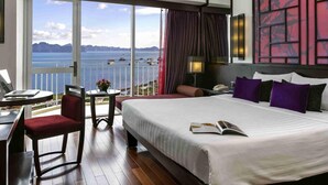 A hotel room with a large bed, a desk with a laptop, a chair, and a view of the sea.