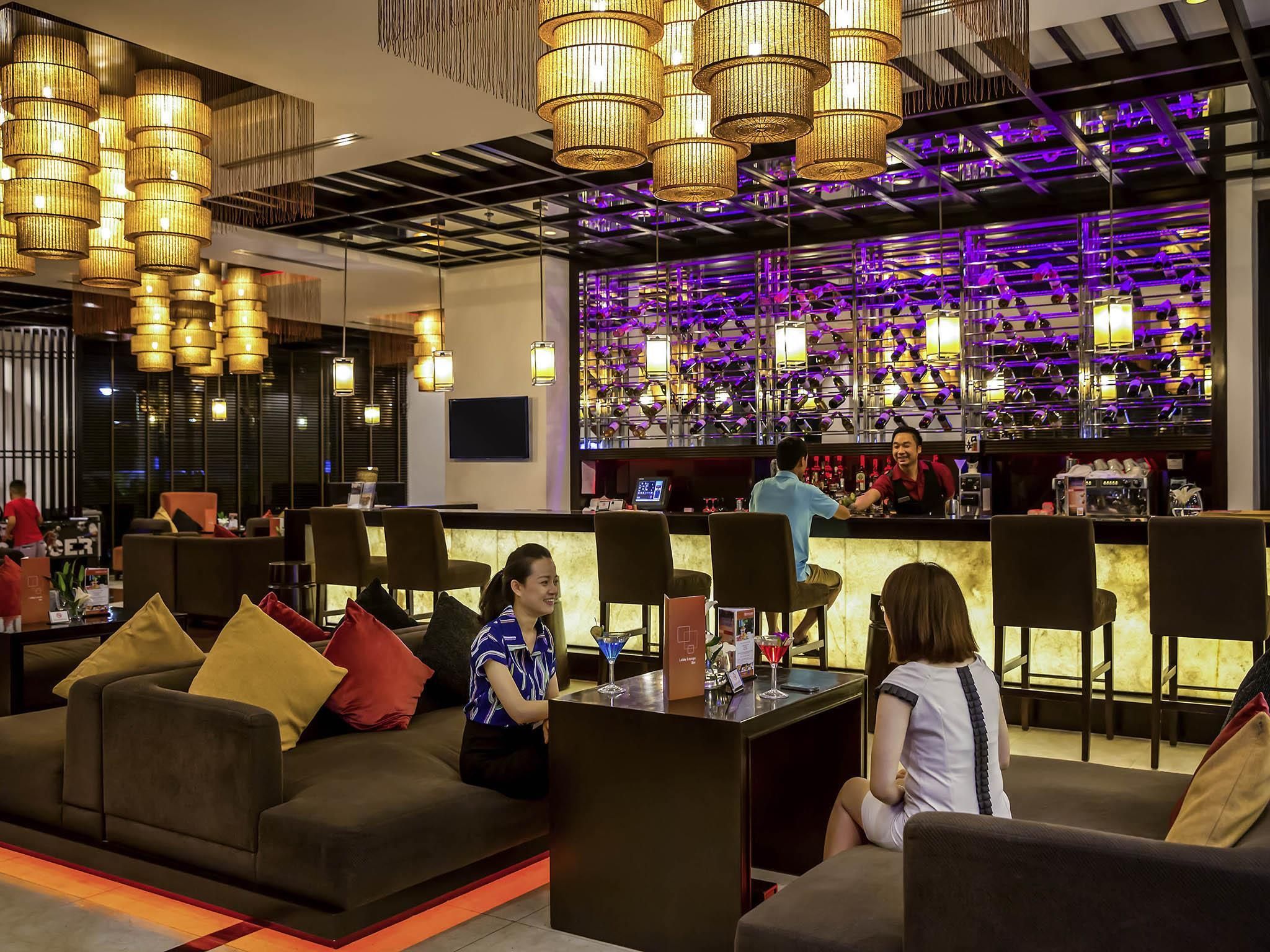 A modern bar area with multiple seating options, including sofas and chairs, and a bar counter with a bartender.
