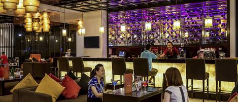 A modern bar area with multiple seating options, including sofas and chairs, and a bar counter with a bartender.