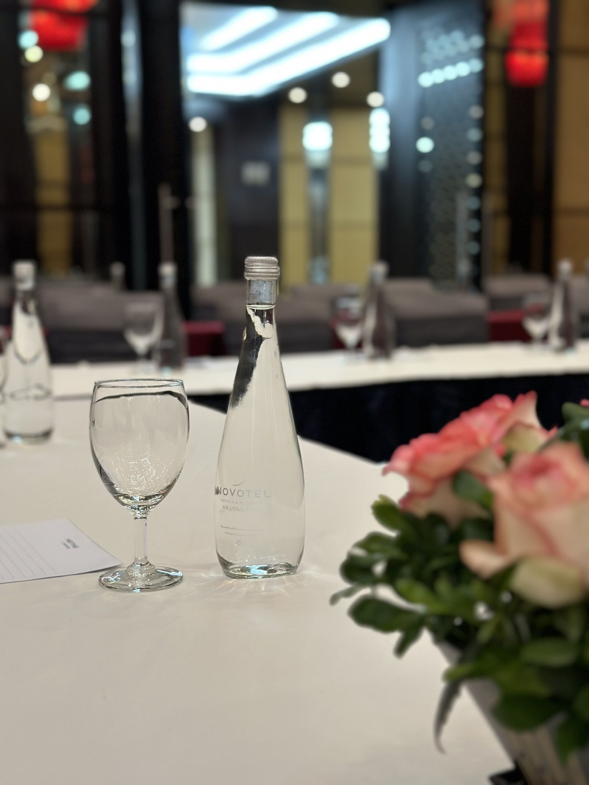 Une table avec une bouteille et un verre, un menu et un vase de fleurs.