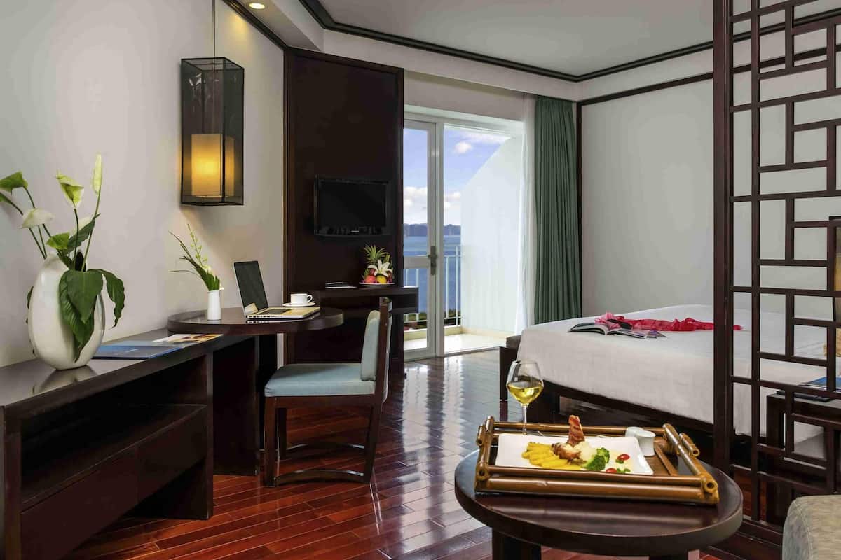 Habitación de hotel con cama, escritorio con una computadora portátil, mesa de comedor con comida y televisor en la pared.