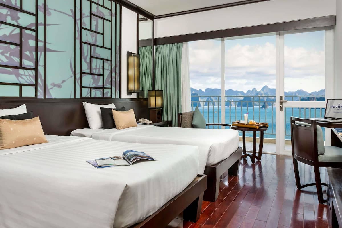 Habitación de hotel con dos camas, un escritorio, una silla, una computadora portátil y vistas al mar.