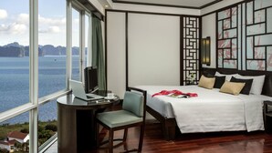 A hotel room with a large window, a bed, a desk with a laptop, and a chair.