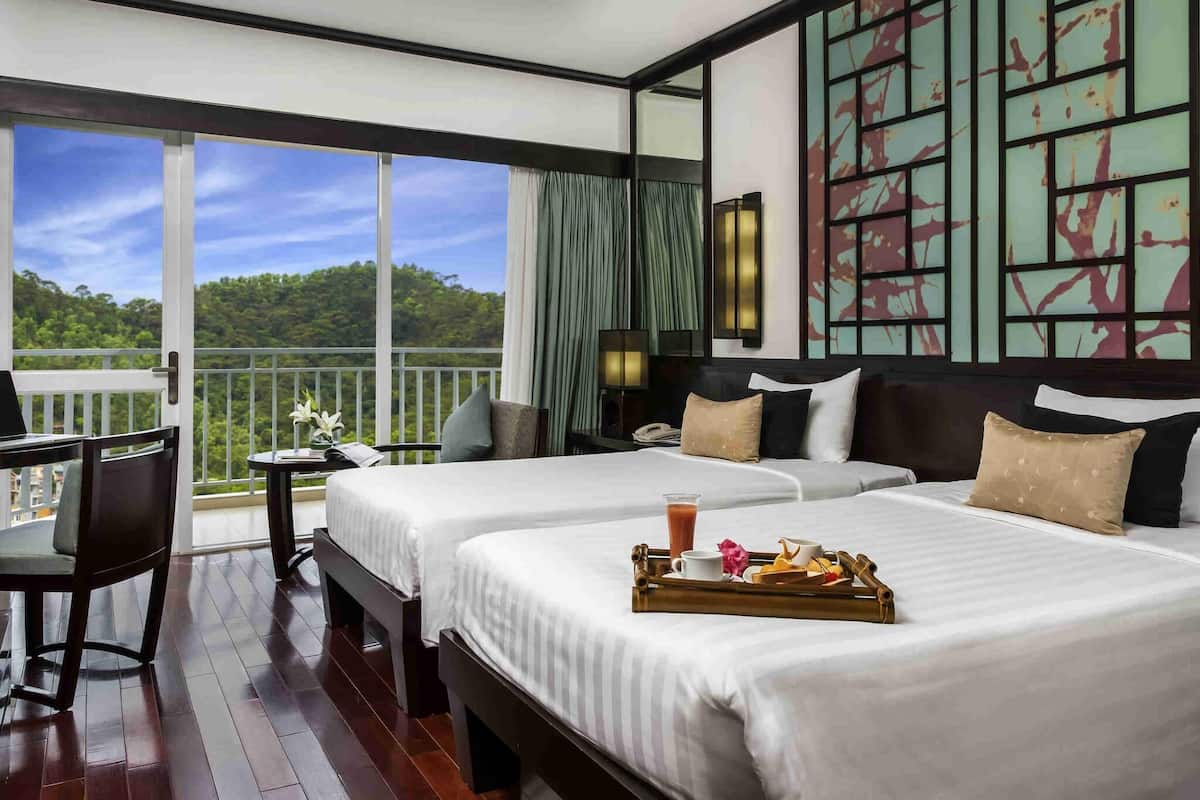 Habitación de hotel con dos camas, un escritorio, un balcón con vistas al bosque y un adorno en la pared.
