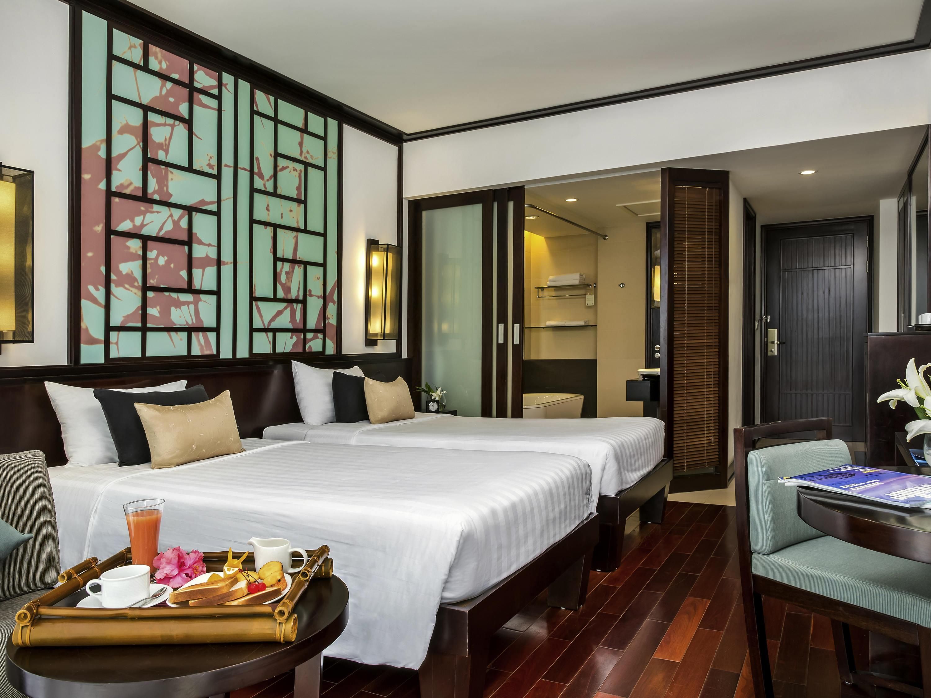 Habitación de hotel con dos camas, zona de comedor, baño y vistas a la ciudad.