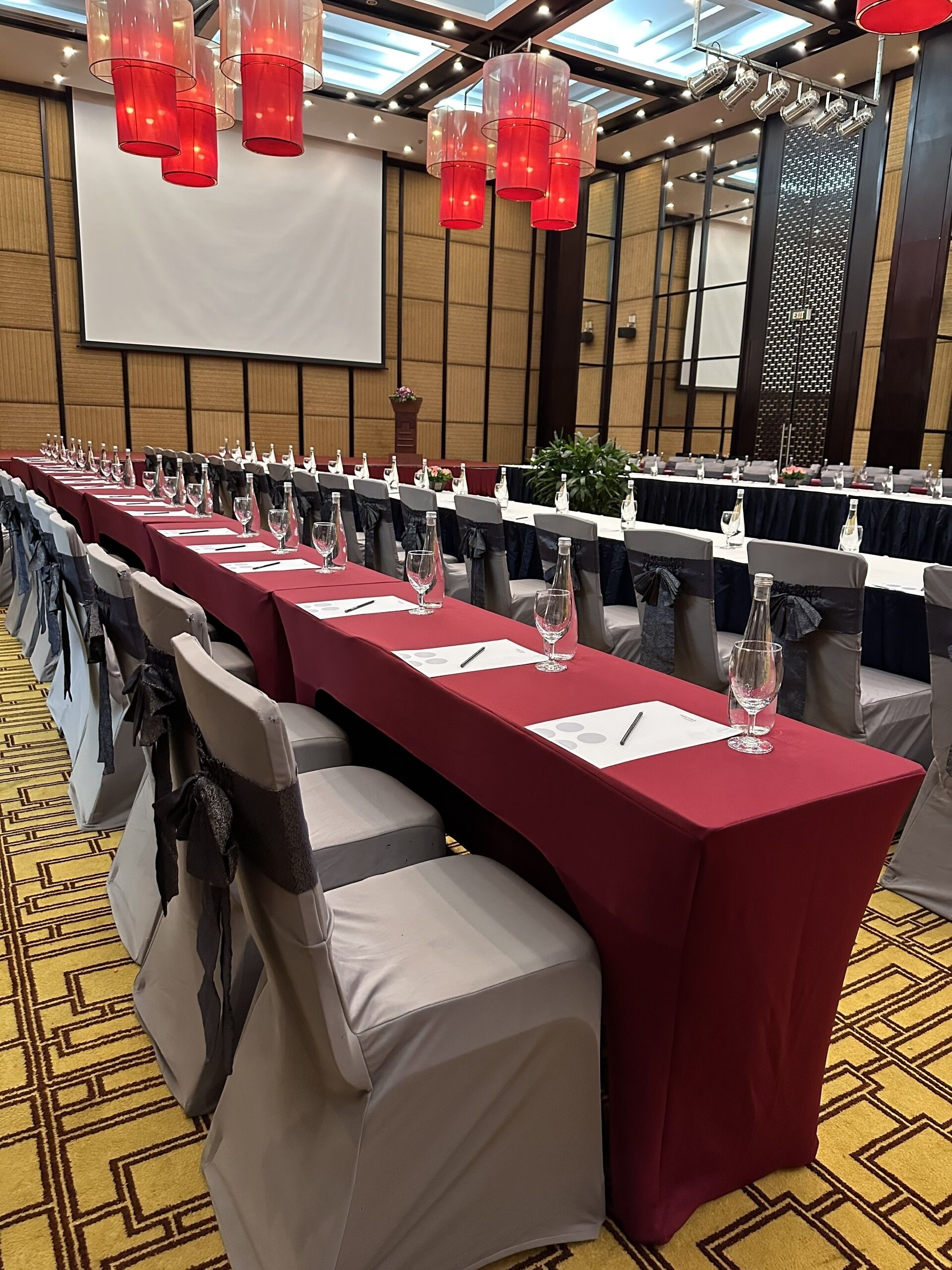 A conference room with long tables, chairs, and red lighting fixtures.