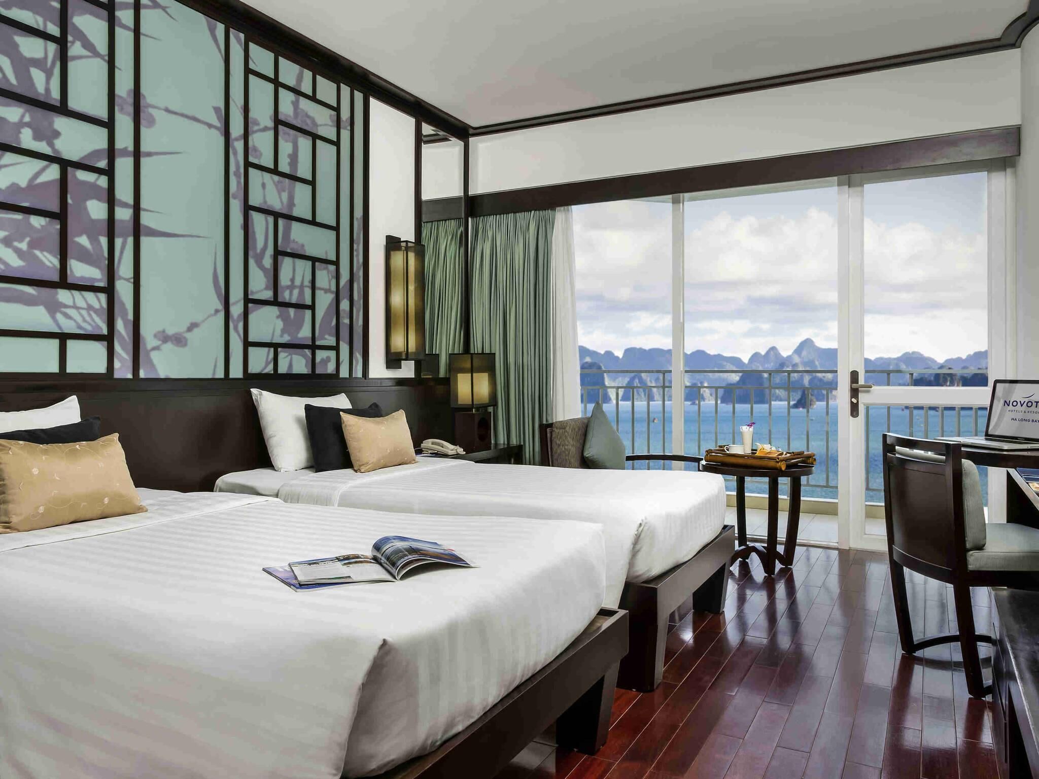 Habitación de hotel con dos camas, un escritorio, una silla y un balcón con vistas al mar.
