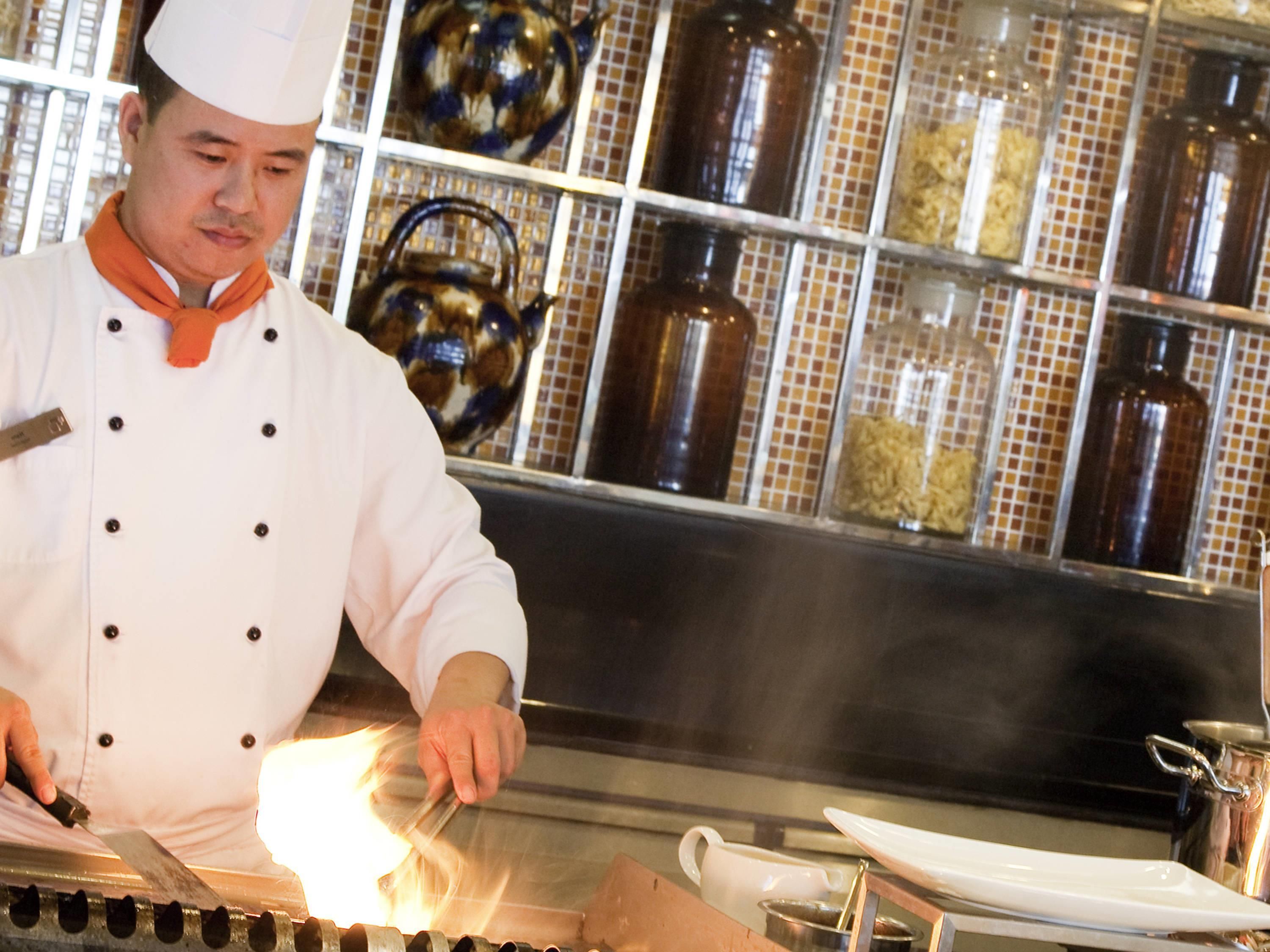 A chef in a white uniform with a hat, working at a stove with a pot of food.