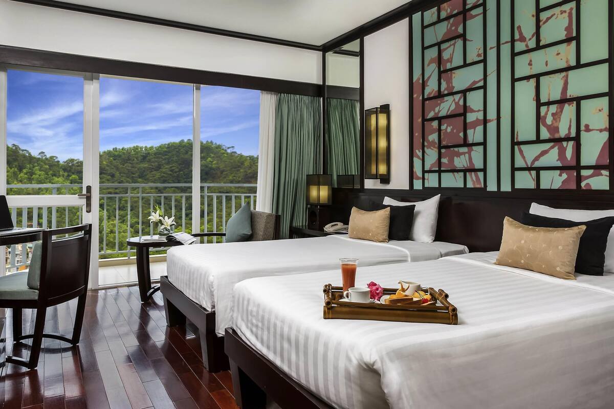 Ein Hotelzimmer mit zwei Betten, einem Schreibtisch, einem Balkon mit Blick auf den Wald und einer Wandverkleidung.