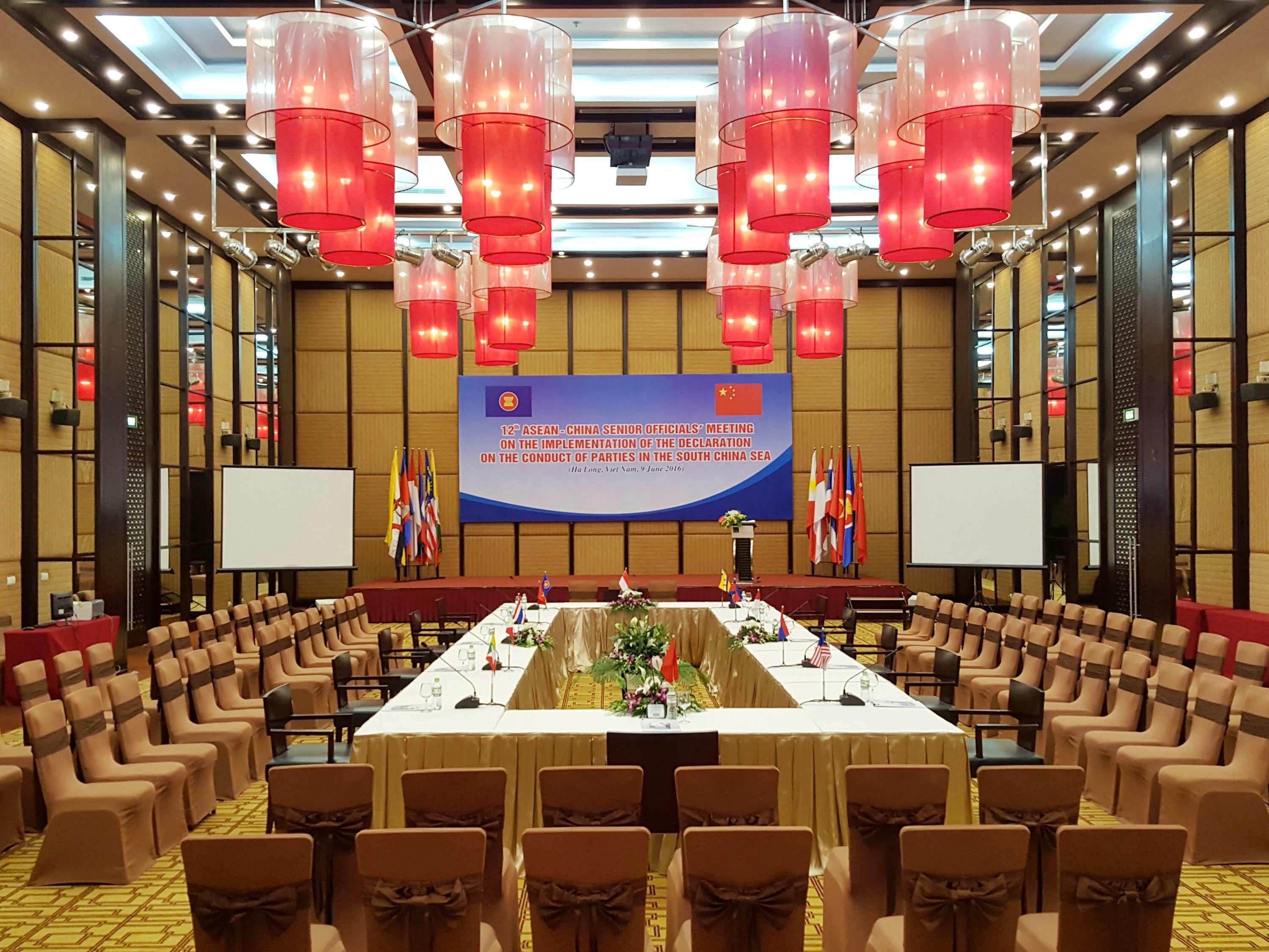 Un salón de conferencias con una larga mesa, sillas, banderas y un banderín.