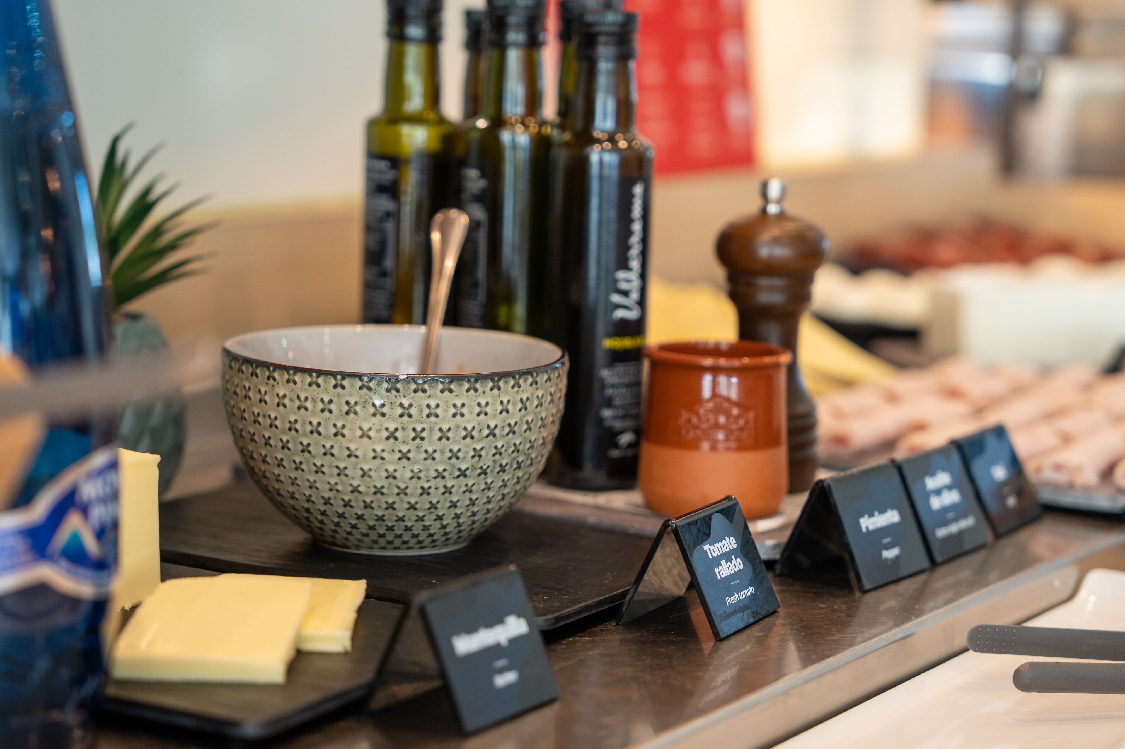 A buffet setup with a patterned bowl, cheese, and labeled dishes.