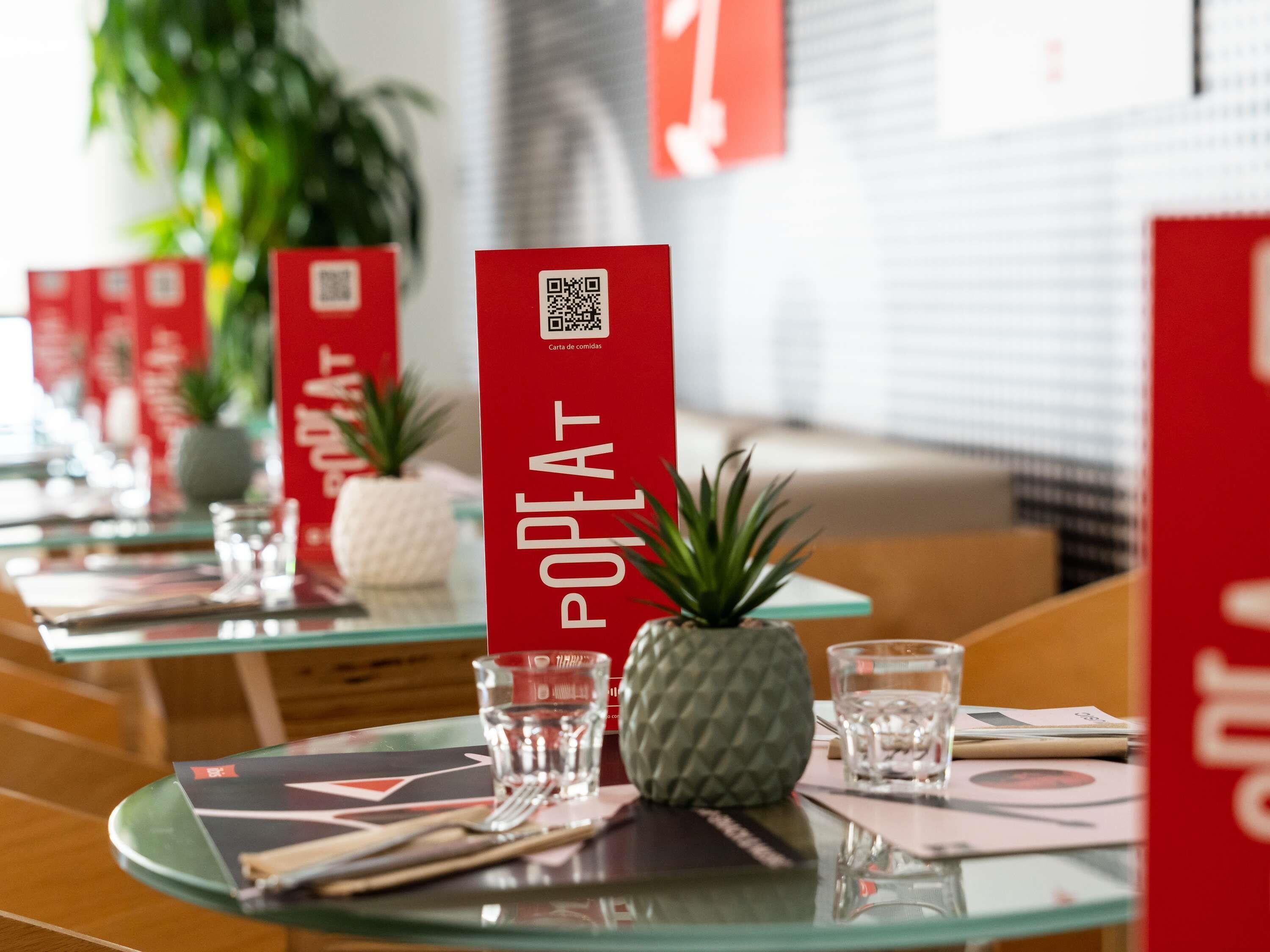 Un restaurant décoré de codes QR sur des panneaux rouges, avec un ananas comme élément central et de la verrerie transparente sur les tables.