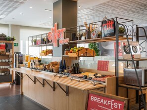 Un área de bufé de desayuno con un letrero 'START MEUP', diferentes alimentos y un reproductor de casetes 'BREAKFASTEST'.