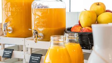 Dos grandes dispensadores de jugo de naranja, una cesta de manzanas y un cartel que indica 'Pineapple juice'.