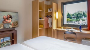 Habitación de hotel con cama, escritorio con silla, armario, televisor y ventana con vistas.